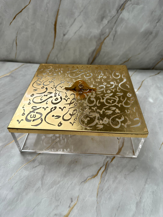 Enhance your decor with our luxurious gold-tone decorative box featuring intricate Arabic calligraphy. This elegant piece doubles as functional storage and a sophisticated accent for any room. Its polished gold finish on the lid pairs beautifully with a transparent acrylic base, blending modern aesthetics with timeless charm. Ideal for gifting or adding a touch of cultural richness to your home, this spacious box is a testament to refined taste and artistic appreciation.