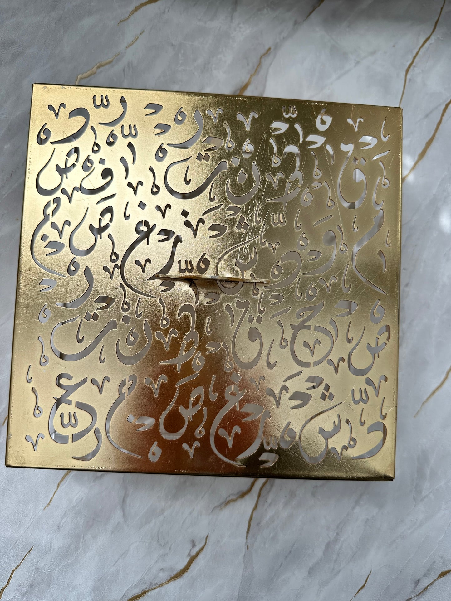 Elevate your space with our stunning gold-tone decorative box, adorned with intricate Arabic calligraphy. This versatile piece serves as both a functional storage solution and an exquisite accent for any room. The polished gold lid contrasts elegantly with the transparent acrylic base, creating a modern yet timeless look. Perfect for gifting or adding cultural flair to your home decor, this spacious box combines luxury with practicality.