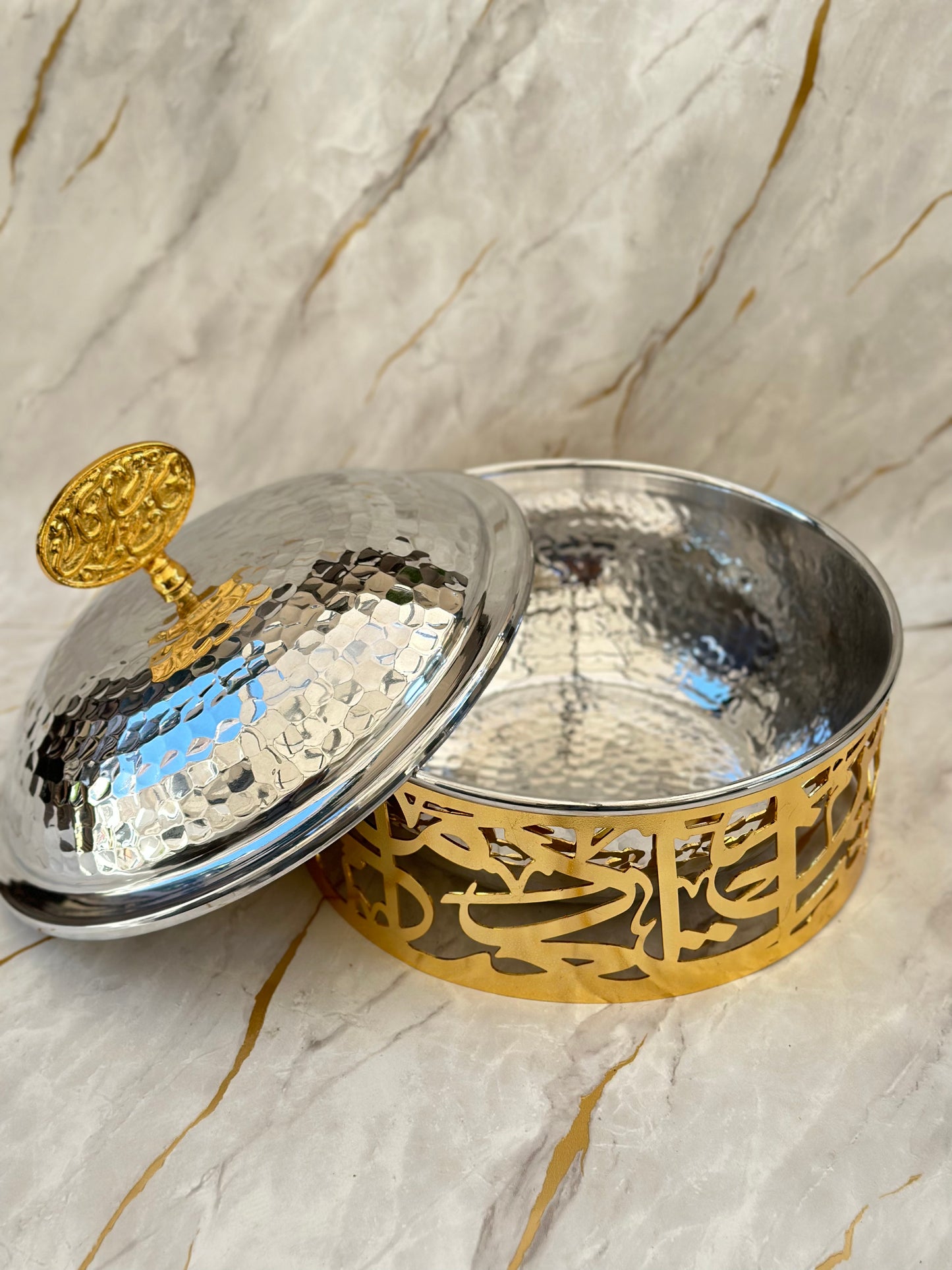 Admire our "Gilded Reflections" Dessert Dome, a blend of tradition and modernity. Its hammered silver dome reflects light, resting atop a golden base adorned with intricate Arabic calligraphy. Perfect for showcasing desserts, it's crowned with an ornate golden knob, making it an ideal centerpiece for festive gatherings or everyday luxury.