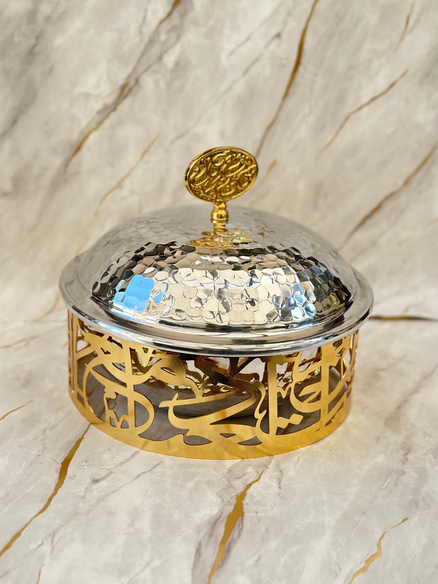 Experience elegance with our "Gilded Reflections" Dessert Dome. Featuring a shimmering hammered silver dome atop a golden base embellished with Arabic calligraphy, this piece not only reflects light beautifully but also serves as a stunning showcase for desserts. Perfect for enhancing your table decor during celebrations or daily indulgences.