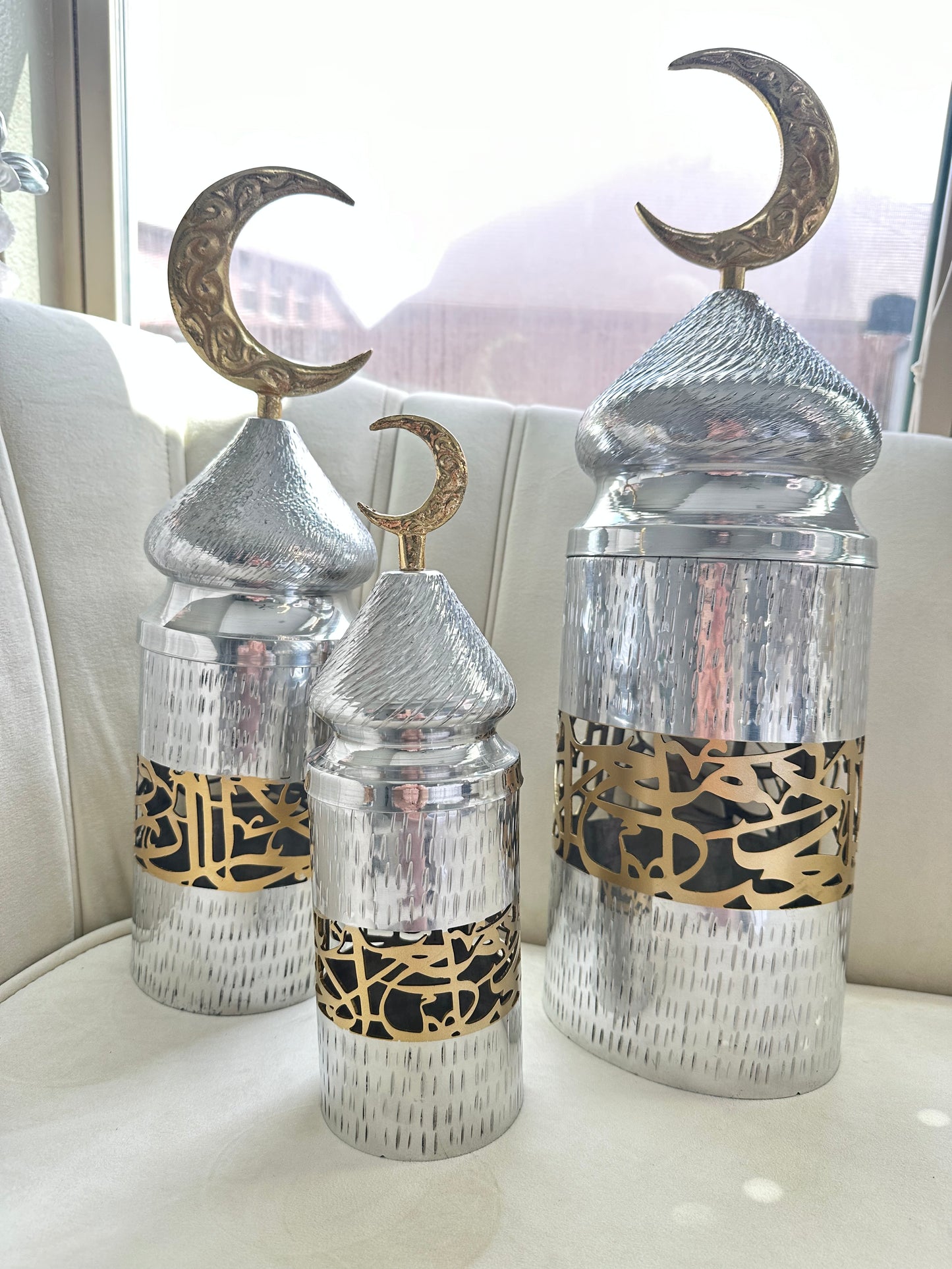  ChatGPT Enhance your decor with our “Crescent Moon Adorned Lantern Canisters.” Crafted from hammered metal, each canister reflects light beautifully. The set of three sizes features intricate Arabic calligraphy and transparent sections for a warm glow. Perfect for any occasion, these canisters blend traditional allure with contemporary sophistication, adding elegance to your home.