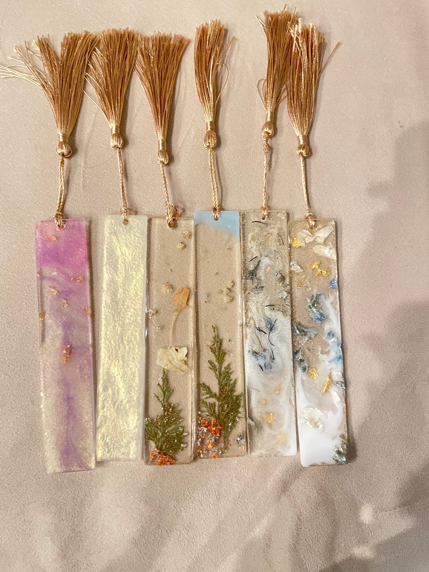 Discover our Handmade Resin Bookmark, a testament to artistic craftsmanship. Each piece features a mesmerizing blend of gold and blue hues, enriched with sparkling glitter details. Hand-poured resin ensures durability and a glossy finish that catches and reflects light beautifully. Complete with a hand-tied tassel, this bookmark is not just a practical accessory but also a stunning decor piece for book enthusiasts and collectors alike.