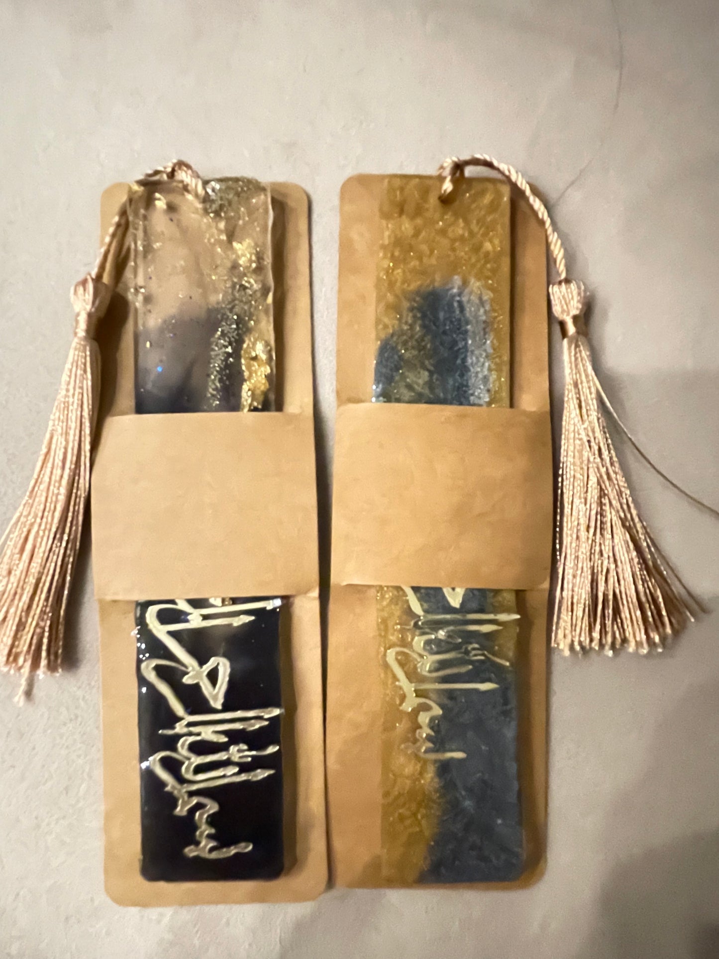 Explore our Handmade Resin Bookmark, a tribute to artistic mastery adorned with intricate Arabic calligraphy. Each piece showcases a captivating fusion of gold and blue tones, accentuated by shimmering glitter. Crafted from durable, hand-poured resin, it boasts a glossy finish that catches and reflects light enchantingly. Ideal for book enthusiasts and collectors seeking both practicality and exquisite décor.